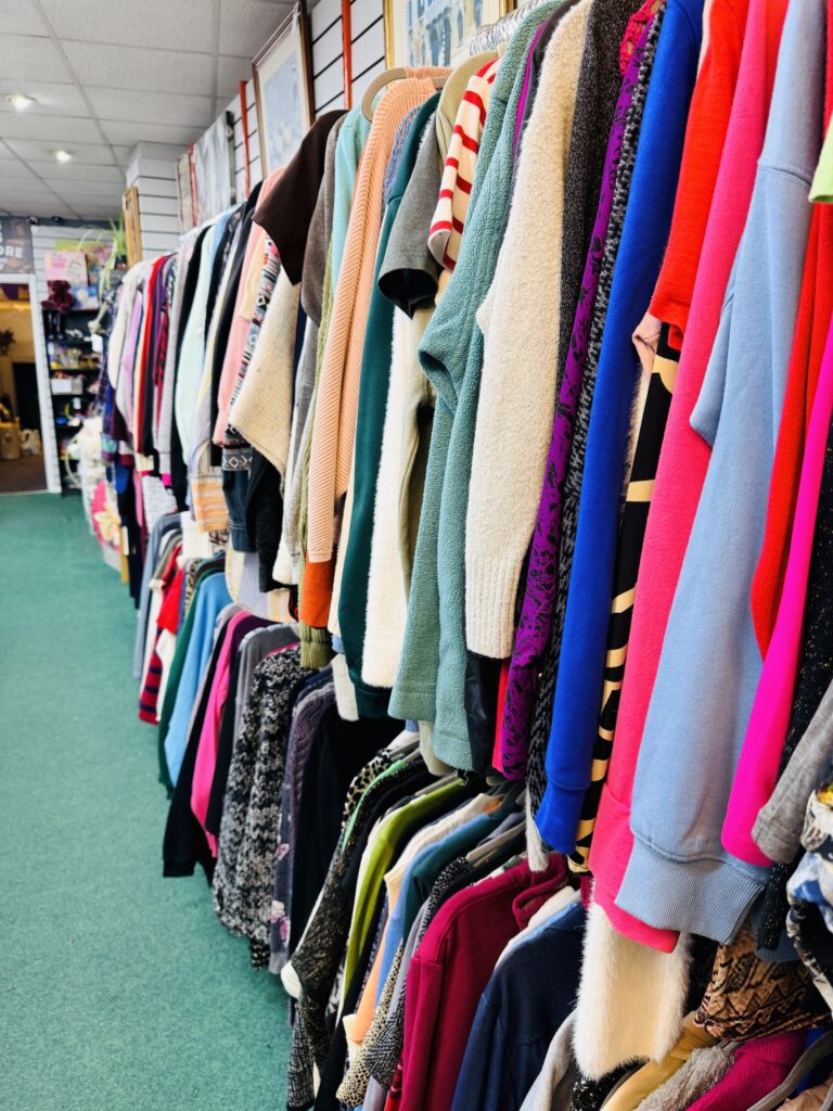 A colourful rack of various jumpers and tops in a clothing shop, with neatly organised garments hanging on hangers along a green carpeted aisle—discover your next favourite look at Hooftastic Finds.